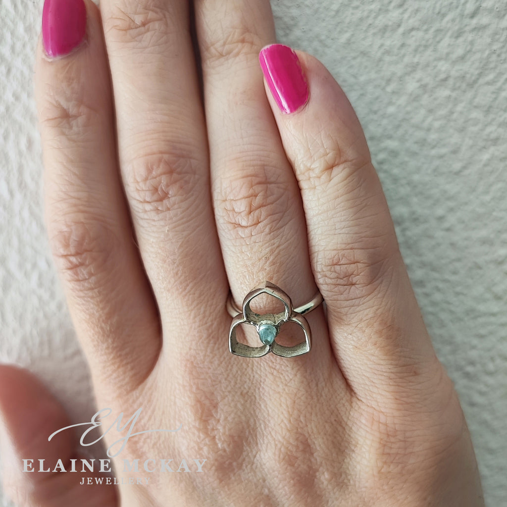 Hand wearing a silver ring with bullet shaped topaz flower design on a neutral background, branded 'Elaine McKay Jewellery