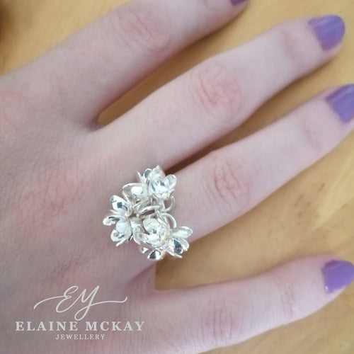 Silver ring with floral design on a hand, branded 'Elaine McKay Jewellery'.