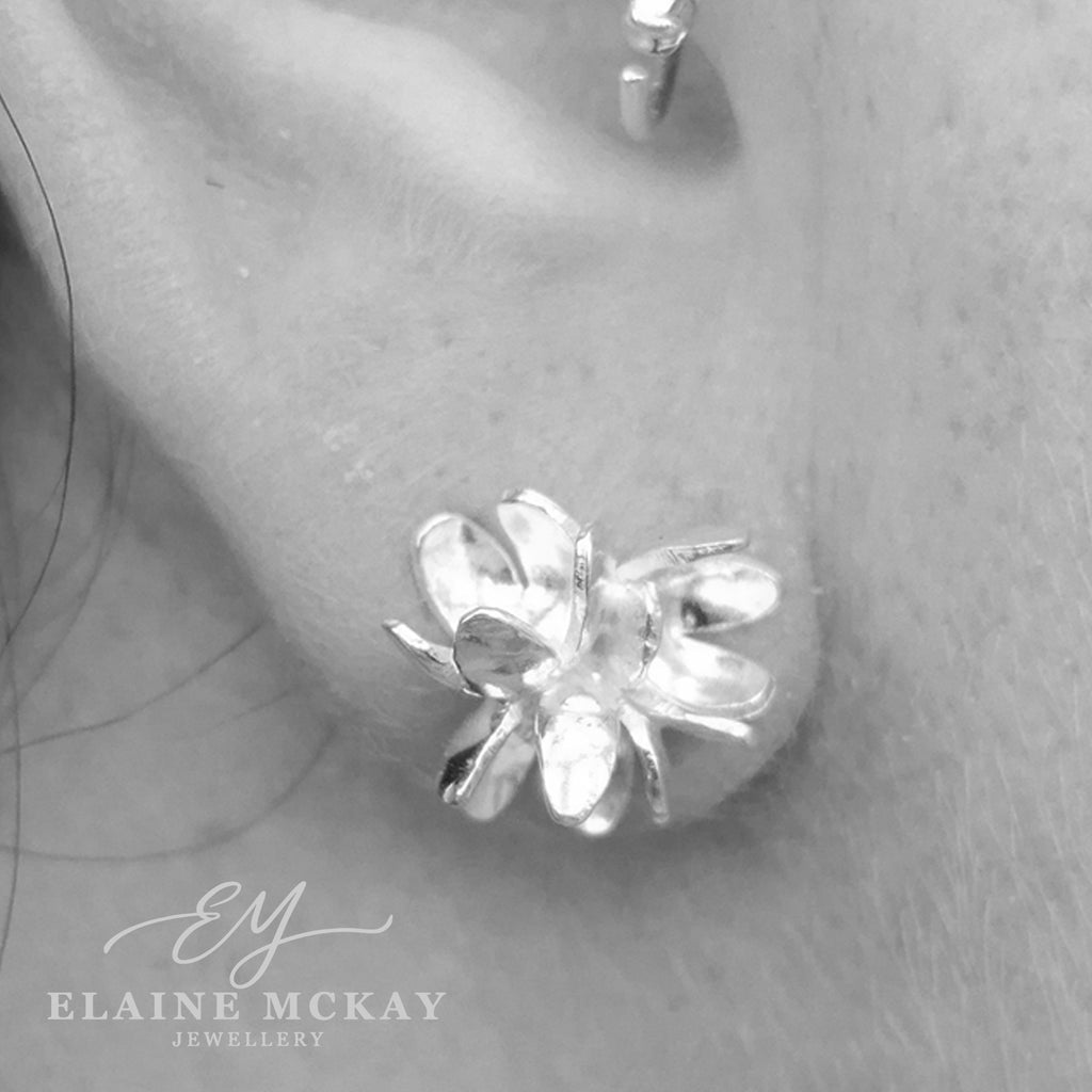 Silver flower-shaped earring worn on an ear with 'Elaine McKay Jewellery' branding.