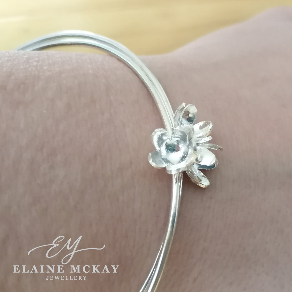 Silver bracelet with a floral design worn on a wrist, branded 'Elaine McKay Jewellery'.