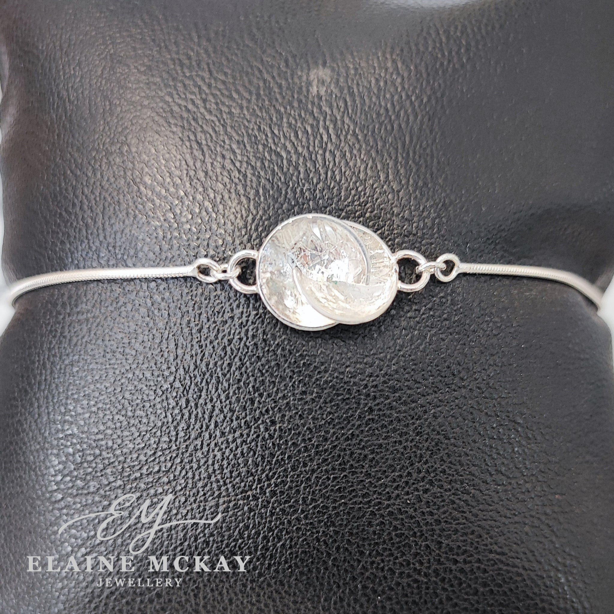 Silver bracelet with a circular design on a black leather surface, branded 'Elaine McKay Jewellery'.