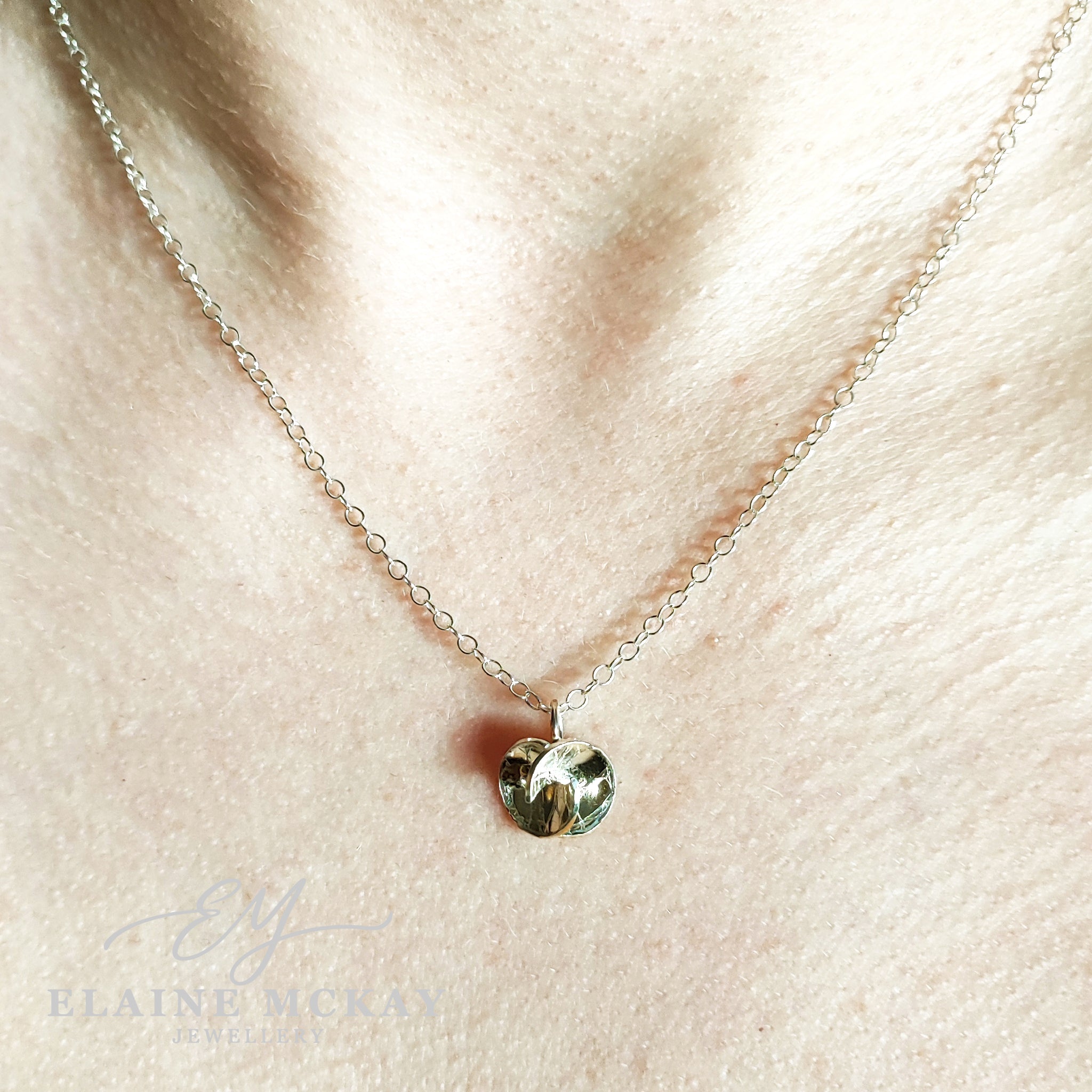 Necklace with a round pendant on a models neck, branded 'Elaine McKay Jewellery