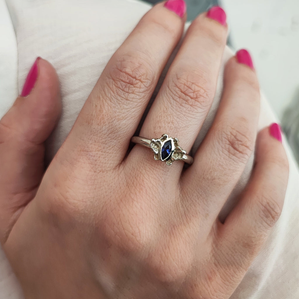 Hand wearing a silver ring with a tanzanite cubic zirconia gemstone, pink nail polish on other fingers.